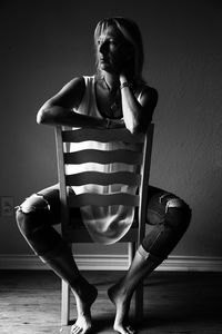 Thoughtful woman sitting on chair against wall at home