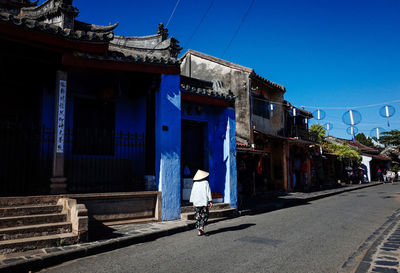 People on street by buildings against blue sky