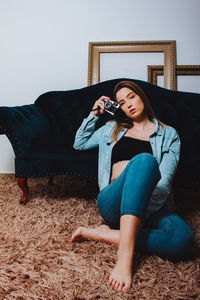 Portrait of woman holding camera sitting by sofa at home