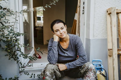 Portrait of smiling female carpenter sitting at entrance of house