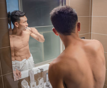 Rear view of shirtless man standing in bathroom