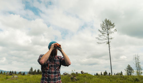 Low angle view of man looking through binoculars on field against sky