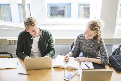 Smiling male and female students studying at desk in classroom