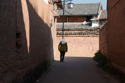 Rear view of man walking on alley amidst buildings in city