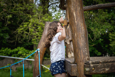 A girl climbs a rope swing on a tree in the park.