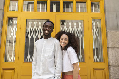 Smiling man and woman in front of yellow door