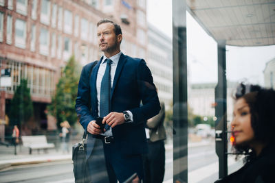 Businessman and businesswoman waiting at bus stop seen from glass