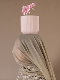 Side view of woman under scarf with flower pot on head against beige background