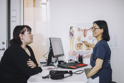 Smiling female doctor explaining to patient while pointing at organ chart in medical clinic