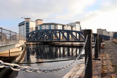 Bridge over river by buildings against sky