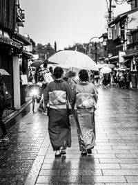Rear view of people walking on wet street during rainy season