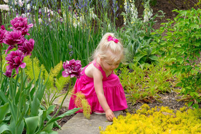 Cute girl wearing pink dress crouching amidst plants