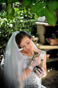 Bride in wedding dress holding cat while sitting at yard