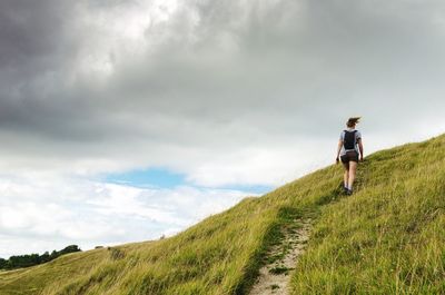 Rear view of woman walking on mountain against cloudy sky