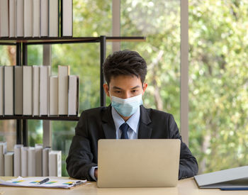 Man with mask using laptop at table in office