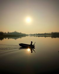 Silhouette man on boat in lake against sky during sunset
