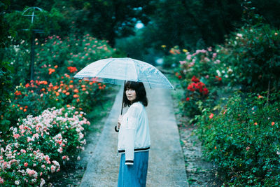 Woman holding umbrella standing by plants during rainy season