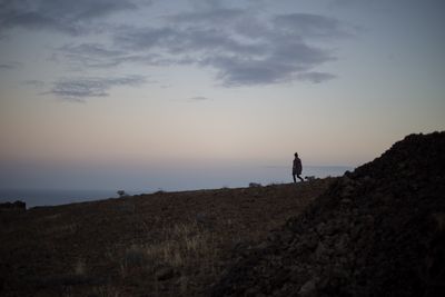 Silhouette man standing on land against sky during sunset