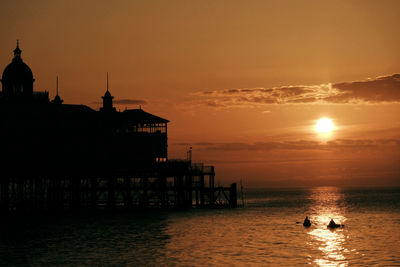Silhouette built structure by sea against sky during sunset