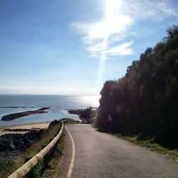 Empty road by sea against cloudy sky