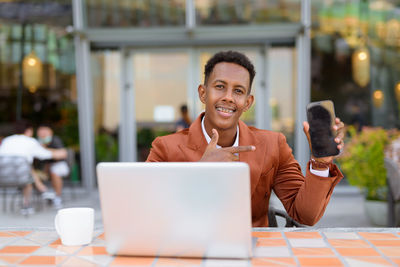 Portrait of businessman showing smart phone at cafe