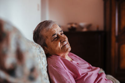 Side view of a senior woman with alzheimer's mental health issues sitting in a sofa alone in her home