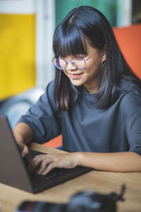 Young woman using mobile phone while sitting on table