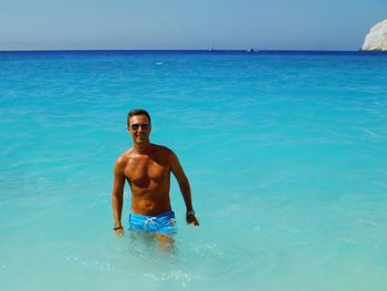 Portrait of shirtless man standing in sea against sky on sunny day