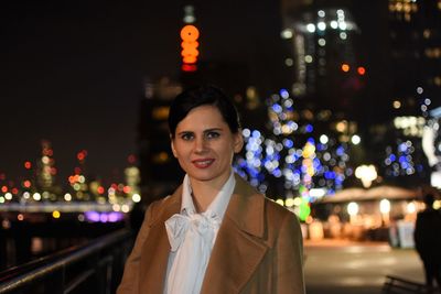 Portrait of smiling young woman in illuminated city at night