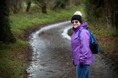 Portrait of smiling woman standing on dirt road in forest