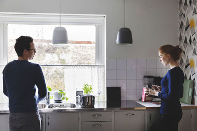 Man washing utensils while woman cooking food in kitchen