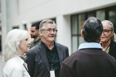 Smiling senior businessman wearing eyeglasses standing with colleagues discussing in convention center