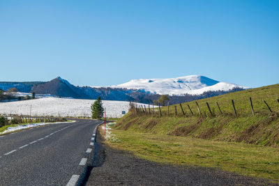 Road leading towards mountains against clear blue sky