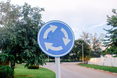 Road sign by trees against sky