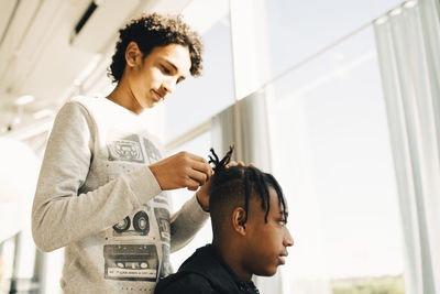 Teenage boy styling friend's hair while standing in restaurant