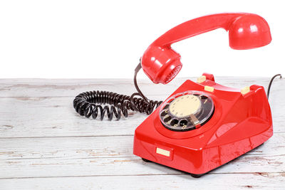 Close-up of red rotary phone on wooden table against white background