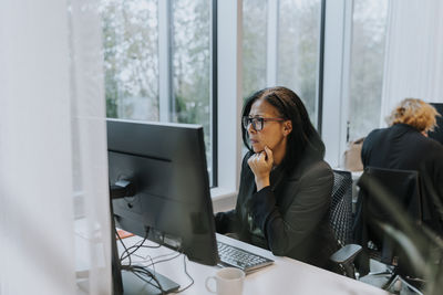 Confident senior businesswoman using computer while sitting with hand on chin at office