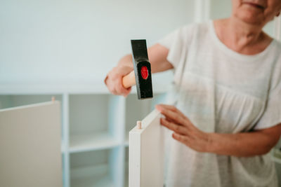 Midsection of man holding camera while standing against wall at home