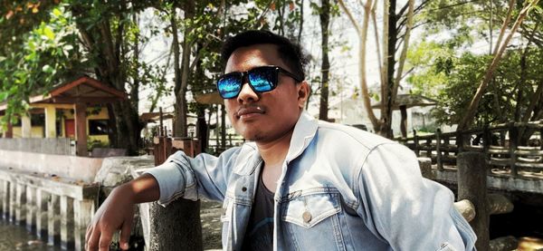 Portrait of young man wearing sunglasses standing against trees