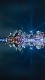 Sydney opera house and modern buildings reflecting on sea in city at night