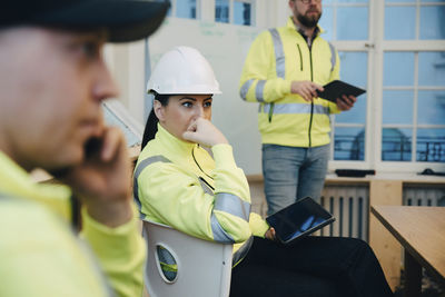 Thoughtful female contractor sitting with digital tablet in office during meeting