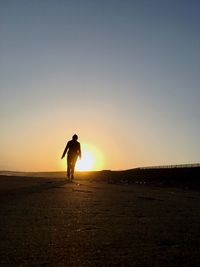 Rear view of silhouette person walking on beach against sky at sunset
