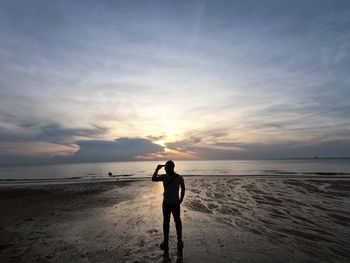 Silhouette man standing on beach against sky during sunset