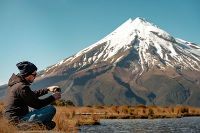 Man sitting on snowcapped mountain against clear sky