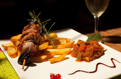 Close-up meat skewer with french fries and ratatouille on table