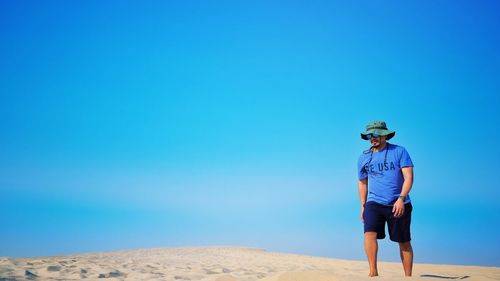 Rear view of man standing on land against clear blue sky