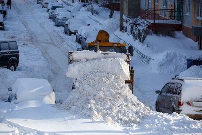 Tractor removing snow from parking near residential building at winter day
