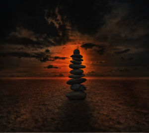 Stacked rocks at beach against cloudy sky at sunset