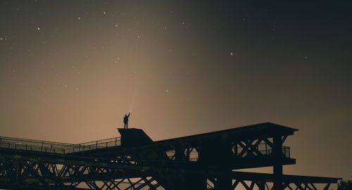 Low angle view of silhouette man on bridge against sky at night