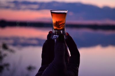 Added a female hand holding a cognac glass against the sky during sunset on the river